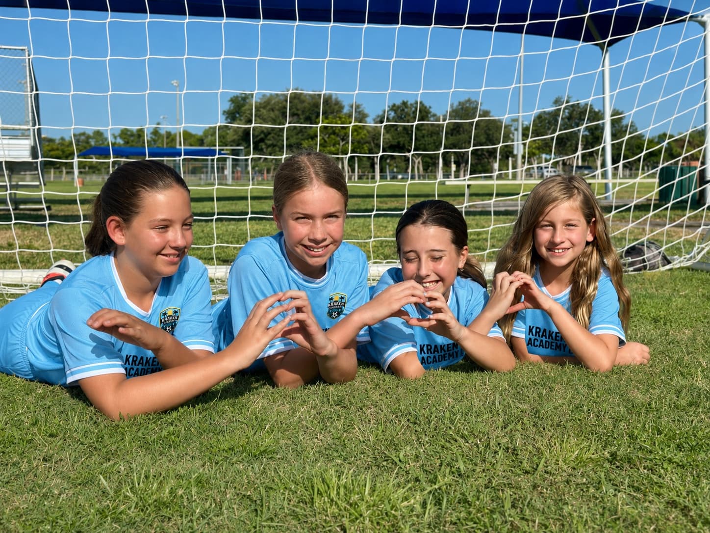 Four Kraken Academy players lying on the grass in the goalmouth, smiling
